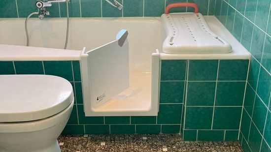Badewannentür mit Wannenbrett in einem grün gefliesten Bad